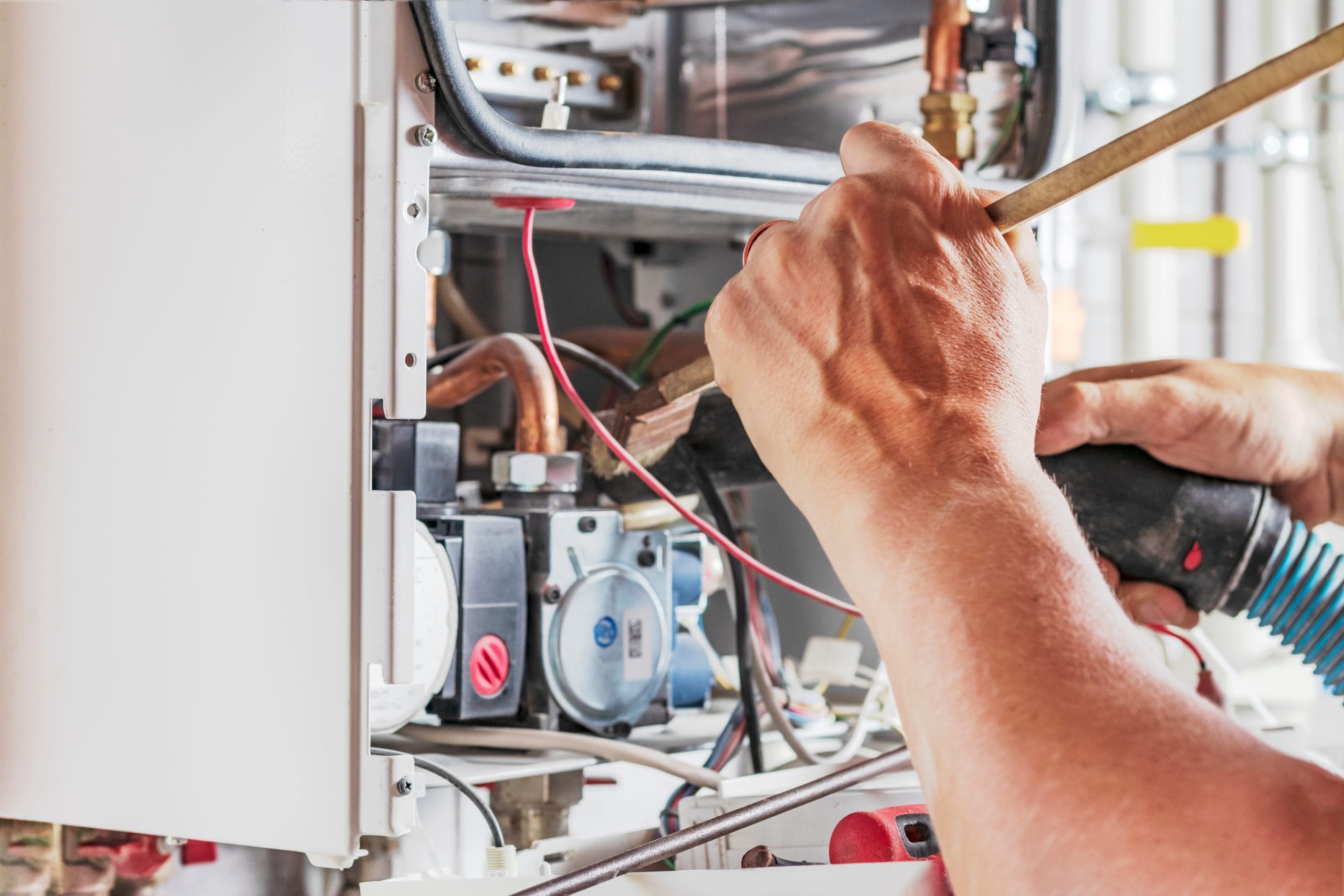 The master sets up a gas boiler, which weighs on the wall. The front dashboard is open. Using a brush and an industrial vacuum cleaner, cleaning from dirt and dirt. Heating System Maintenance Hands working on the wiring of an open appliance or machine with various wires and components visible.