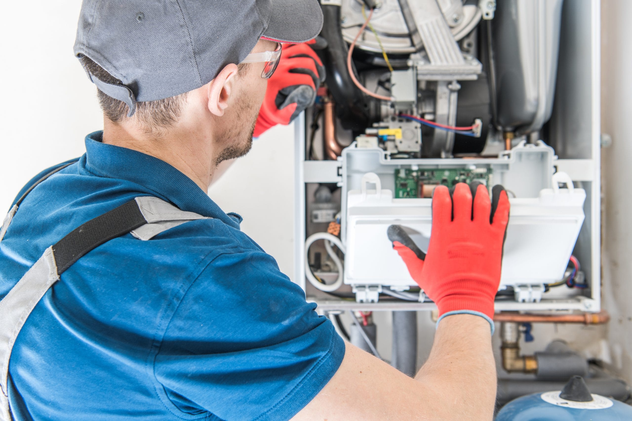 Heating Central Gas Furnace Heat Pump or Furnace? Technician in a blue uniform and red gloves inspecting a furnace control panel.