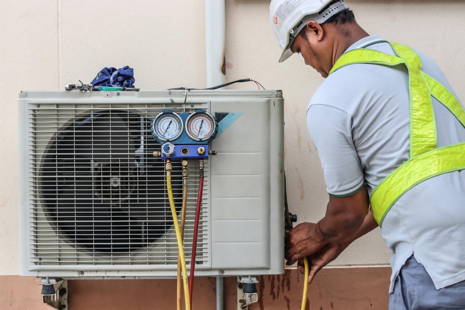 1609-min A technician in safety gear repairs an outdoor air conditioning unit using pressure gauges.